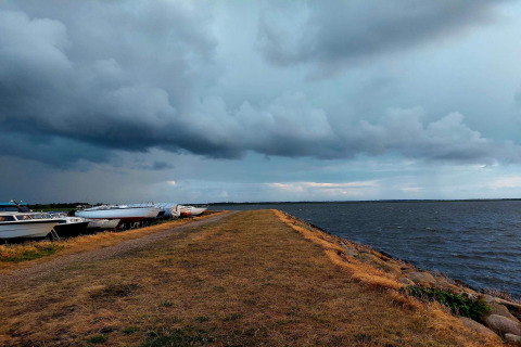 Boote liegen am Ufer eines Sees neben einer Lodge, während sich dunkle Wolken am Himmel sammeln.