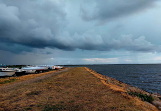 Boote liegen am Ufer eines Sees neben einer Lodge, während sich dunkle Wolken am Himmel sammeln.