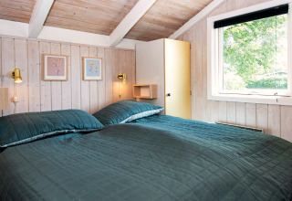 Slaapkamer in Secluded Harbor Cottage in Denemarken met tweepersoonsbed, houten wanden en groot raam.