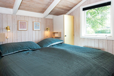 Schlafzimmer im Secluded Harbor Cottage in Dänemark mit Doppelbett, Fenstern und Holzwänden.