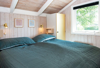 Slaapkamer in Secluded Harbor Cottage in Denemarken met tweepersoonsbed, houten wanden en groot raam.