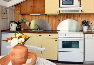 Knusse keuken in Secluded Harbor Cottage in Denemarken met houten panelen, oven, magnetron en bloemenvaas.