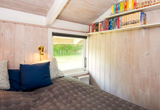 Slaapkamer in Secluded Harbor Cottage in Denemarken met houten wanden, boekenplank en gezellig bed.