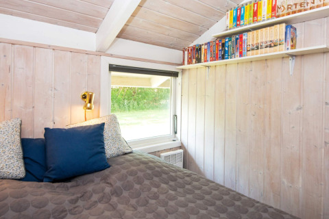Schlafzimmer im Secluded Harbor Cottage in Dänemark mit Holzverkleidung, Bücherregal und Bett.