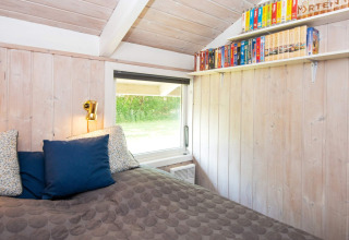 Slaapkamer in Secluded Harbor Cottage in Denemarken met houten wanden, boekenplank en gezellig bed.
