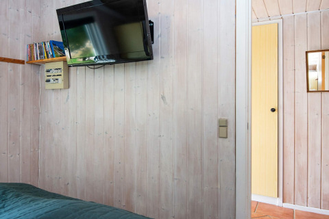 Kamer in Secluded Harbor Cottage, Denemarken, met wand-tv, boekenplank en open deur naar de gang.