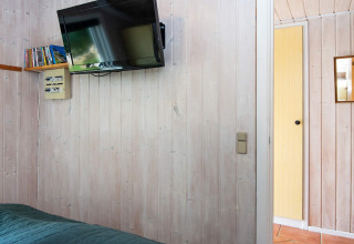 Kamer in Secluded Harbor Cottage, Denemarken, met wand-tv, boekenplank en open deur naar de gang.