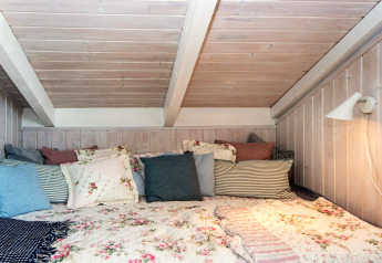 Hyggeligt soverum i «Secluded Harbor Cottage» i Danmark med blomstrede tæpper og mange puder.