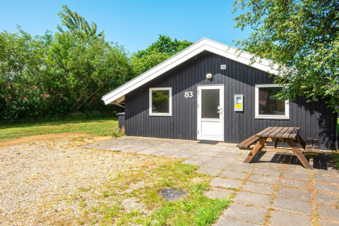 Gezellige Secluded Harbor Cottage in Denemarken met houten picknicktafel en zwarte buitengevel, omgeven door groen.