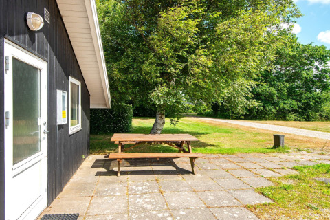 Sitzbereich im Freien an einer dunklen Holzhütte mit Picknicktisch und Blick auf Natur in Dänemark.