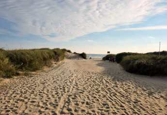 Sti gennem klitterne til stranden nær feriehuset i Blåvand, Danmark, under en lys blå himmel.