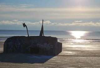Foto di un vecchio bunker con graffiti sulla spiaggia di Blåvand, Danimarca, al tramonto sul mare.