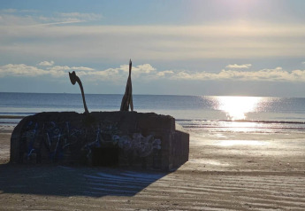 Photo d’un ancien bunker couvert de graffitis sur la plage de Blåvand, Danemark, au coucher du soleil.