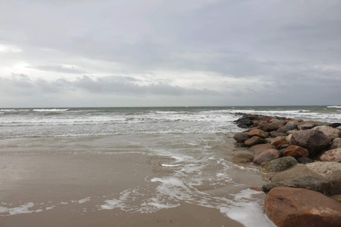 Rotsachtige golfbreker in zee onder bewolkte lucht op het strand bij Blåvand, Denemarken.