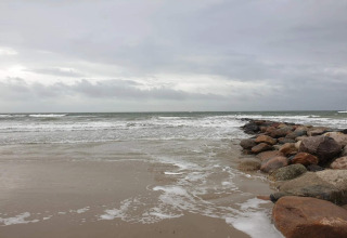 Felsenmole am Ufer mit Wellen und bewölktem Himmel bei Blåvand in Dänemark.
