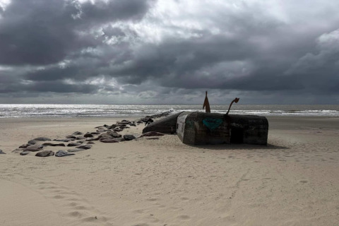 Strand in Blåvand, Denemarken met historische bunker, donkere wolken en stenen pad richting de zee.