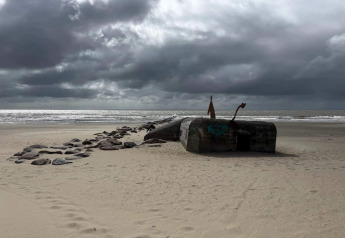 Spiaggia di Blåvand in Danimarca, bunker storico, sentiero di rocce e cielo nuvoloso sopra il mare.
