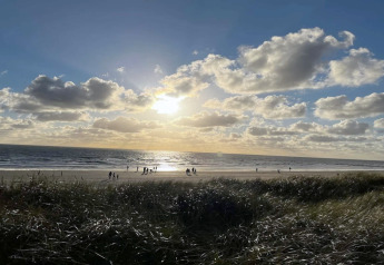 Solnedgang over stranden ved Blåvand, Danmark, set fra hytten '6 personers feriehus', med folk på sandet.