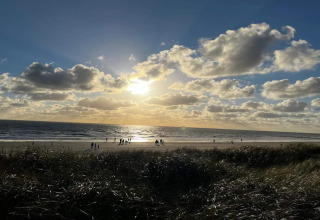 Zonsondergang boven het strand van Blåvand, Denemarken, gezien vanaf het 6 persoons vakantiehuis, met mensen op het zand.