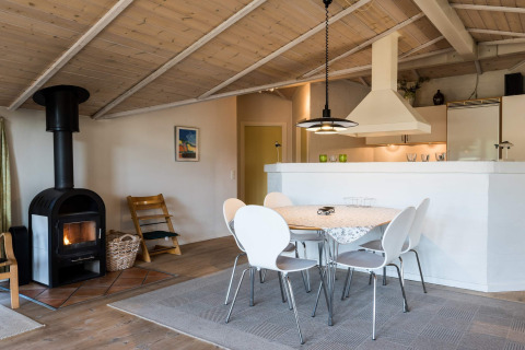 Gemütlicher Wohnbereich mit Esstisch, Holzofen und offenem Küchenbereich in einem Ferienhaus in Blåvand, Dänemark.