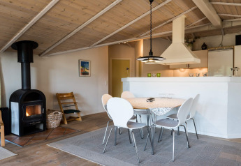 Lyst og hyggeligt opholdsrum med spisebord, brændeovn og åbent køkken i feriebolig i Blåvand, Danmark.
