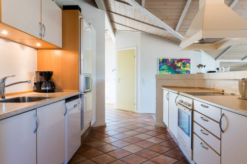 Cucina moderna in una casa vacanze a Blåvand, Danimarca, con armadietti bianchi e dipinto colorato.