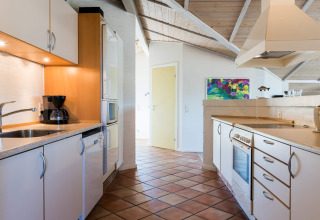 Moderne Küche in einem Ferienhaus in Blåvand, Dänemark, mit weißen Schränken und buntem Gemälde.