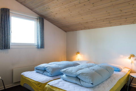 Slaapkamer met schuin houten plafond, twee bedden met geel linnengoed in vakantiehuis in Blåvand, Denemarken.