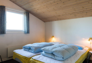 Camera da letto con soffitto in legno inclinato, due letti con lenzuola gialle in casa vacanze a Blåvand, Danimarca.