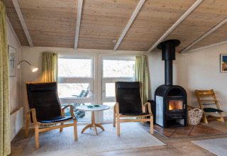Soggiorno di casa vacanze a Blåvand, Danimarca, con stufa a legna, poltrone e soffitto in legno.