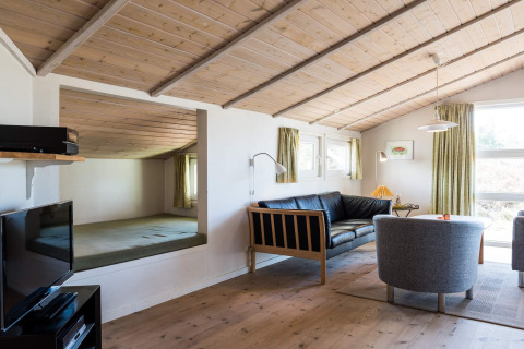 Soggiorno di una casa vacanze a Blåvand, Danimarca, con soffitto in legno, divano e poltrone moderne.
