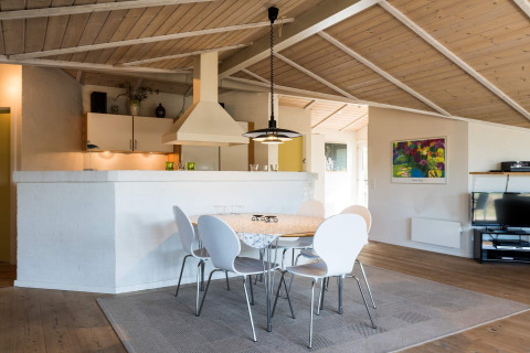 Cucina e zona pranzo luminose in un lodge moderno a Blåvand, Danimarca, con sedie bianche e soffitto in legno.