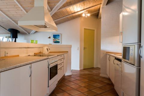 Moderne Küche in einem Ferienhaus in Blåvand, Dänemark, mit weißen Schränken und Holzbalkendecke.