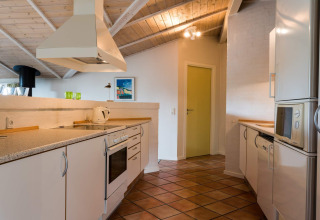 Cucina moderna in una casa vacanza a Blåvand, Danimarca, con armadi bianchi e soffitto in legno.