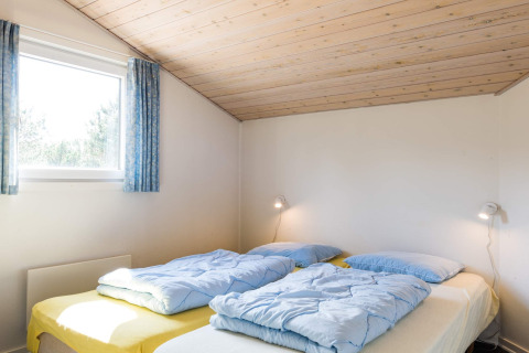 Camera con due letti, piumoni azzurri e soffitto in legno in casa vacanze per 6 persone a Blåvand, Danimarca.