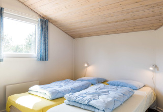 Schlafzimmer mit zwei Betten, blauen Decken und Holzdecke im 6-Personen-Ferienhaus in Blåvand, Dänemark.