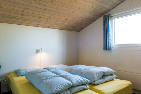 Schlafzimmer mit gelbem Bett, blauen Decken und Holzdecke in einem Ferienhaus in Blåvand, Dänemark.