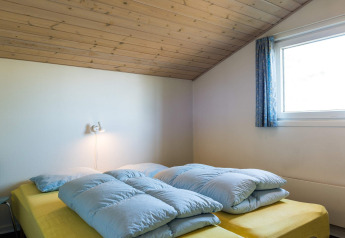 Chambre avec lit jaune, couettes bleues et plafond boisé dans une maison de vacances à Blåvand, Danemark.