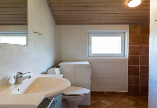 Bagno moderno con lavandino, WC e finestra in casa vacanza per 6 persone a Blåvand, Danimarca.