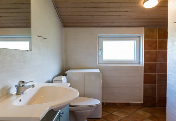 Salle de bain moderne avec lavabo, toilettes et fenêtre dans une maison de vacances à Blåvand, Danemark.