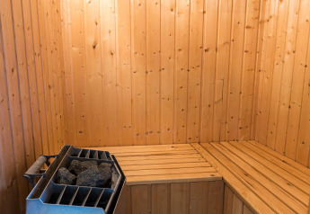 Traditionelle Holzsauna mit Ofen und Steinen in einem 6-Personen-Ferienhaus in Blåvand, Dänemark.