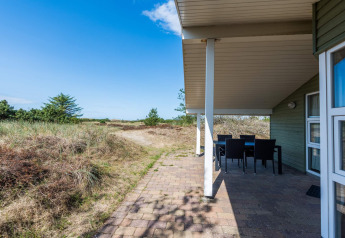 Überdachte Terrasse mit Sitzbereich an einem Ferienhaus in Blåvand, Dänemark, mit Blick auf Dünenlandschaft.