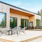 Buitenterras van Cozy Sea House met moderne stoelen en uitzicht op het bos en een blauwe lucht.