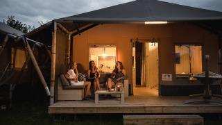 Tres mujeres descansan en la terraza de una tienda safari en Holiday park De Boshoek, Países Bajos, al atardecer.