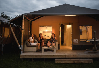 Tre donne si rilassano sulla veranda di una tenda safari al Holiday park De Boshoek nei Paesi Bassi di sera.