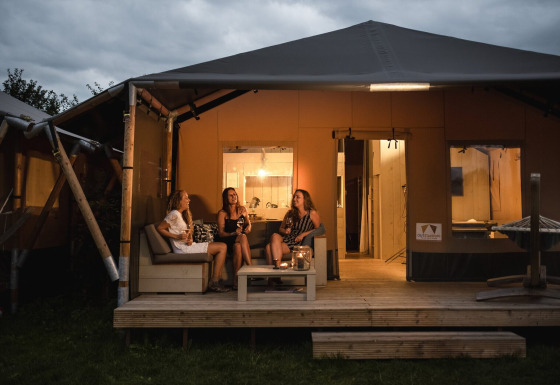 Drie vrouwen genieten ’s avonds op het terras van een safaritent bij Holiday park De Boshoek in Nederland.