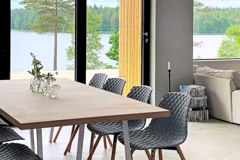 Moderne spiseplads med grå stole, store vinduer og udsigt over søen, indrettet i Cozy Sea House, Sverige.