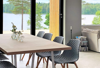 Moderne spiseplads med grå stole, store vinduer og udsigt over søen, indrettet i Cozy Sea House, Sverige.