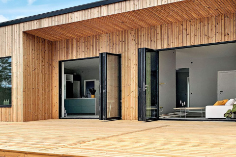 Udendørs udsigt over Cozy Sea House med gæstehytte i Sverige, moderne træfacade og store glasdøre.
