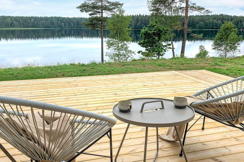 Terrasse med moderne stole og bord, udsigt over fredfyldt sø og skov ved Cozy Sea House i Sverige.